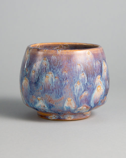 WINDY CUP 'NEBULA', handmade stoneware cup without a handle by Studio 517. Glossy lavender violet with streaks of white and pale blue running down the walls, dotted with small ochre drops that each leave a white trail, like comets in a night sky.
