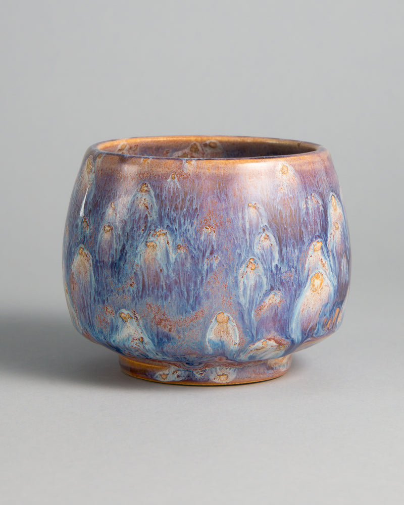 WINDY CUP 'NEBULA', handmade stoneware cup without a handle by Studio 517. Glossy lavender violet with streaks of white and pale blue running down the walls, dotted with small ochre drops that each leave a white trail, like comets in a night sky.