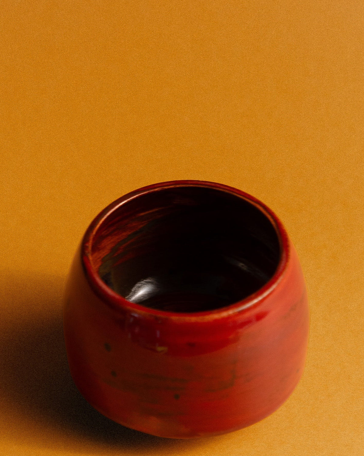 WINDY handmade stoneware cup by Studio 517: one glossy deep red cup standing alone on a flat orange background, with a soft shadow falling to the left.